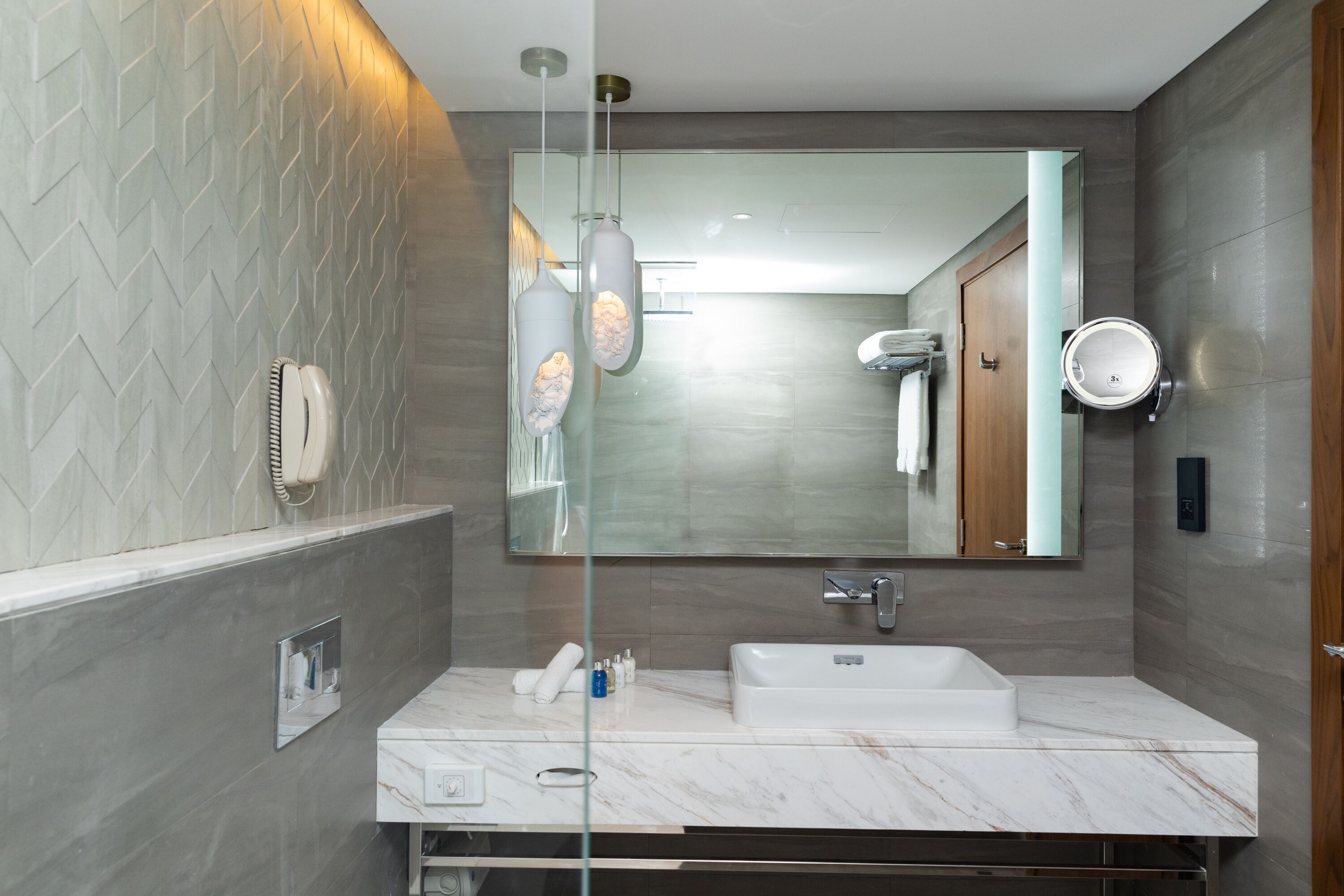 Une salle de bain moderne avec un lavabo en marbre, un grand miroir et une douche à parois de verre.