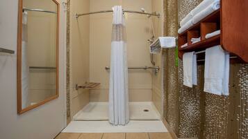 A walk-in shower with a glass door, a wooden shelf with towels, and a mirror on the left wall.