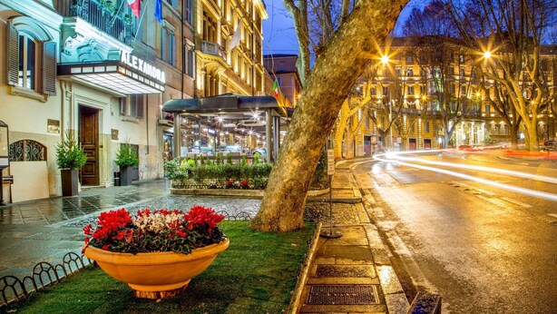 A well-lit urban street with a theater marquee, a bus stop, and a large planter with flowers. - Hotel Alexandra (Rome)