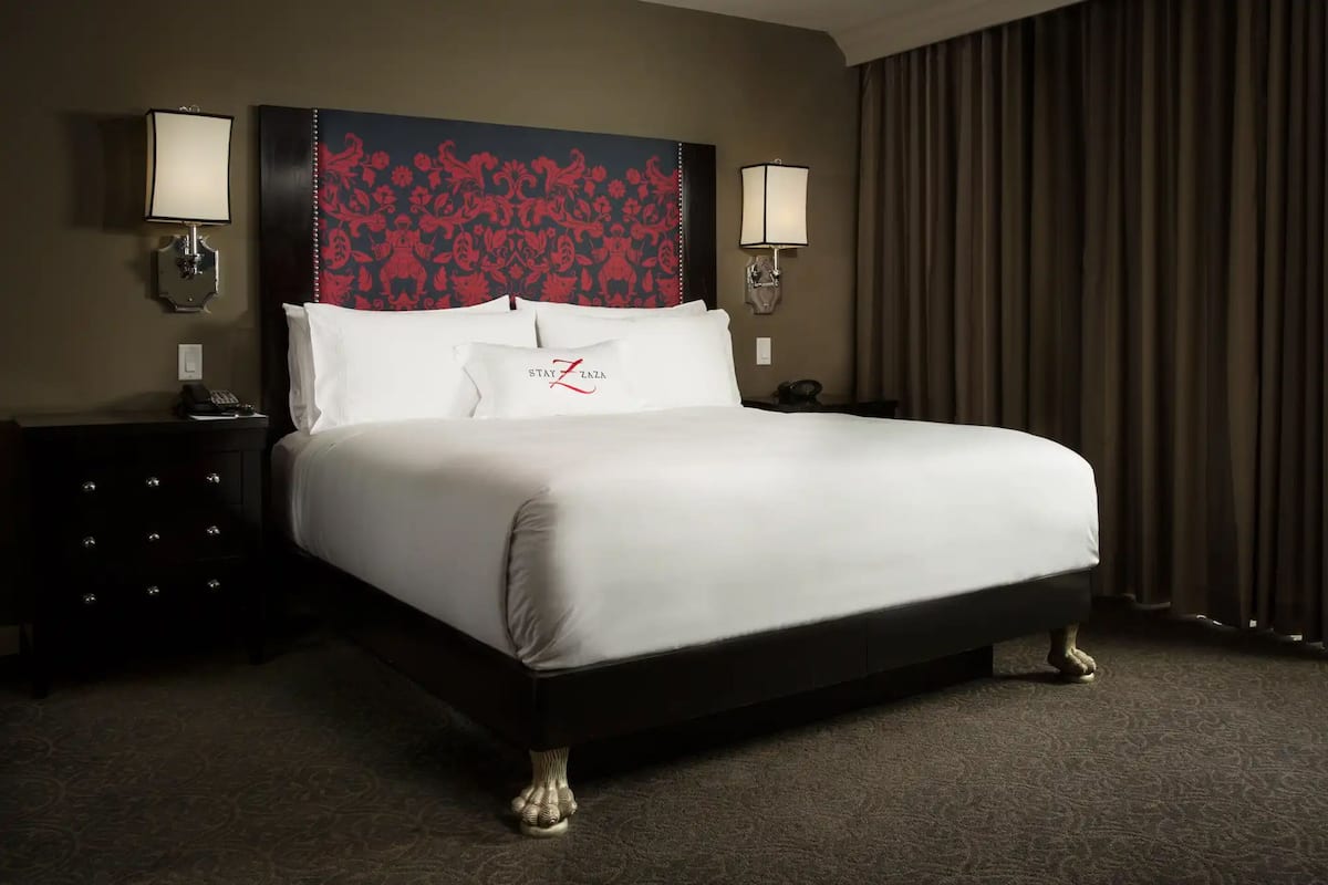 A hotel room with a large bed, two bedside lamps, a telephone, a dark dresser, and a patterned carpet.