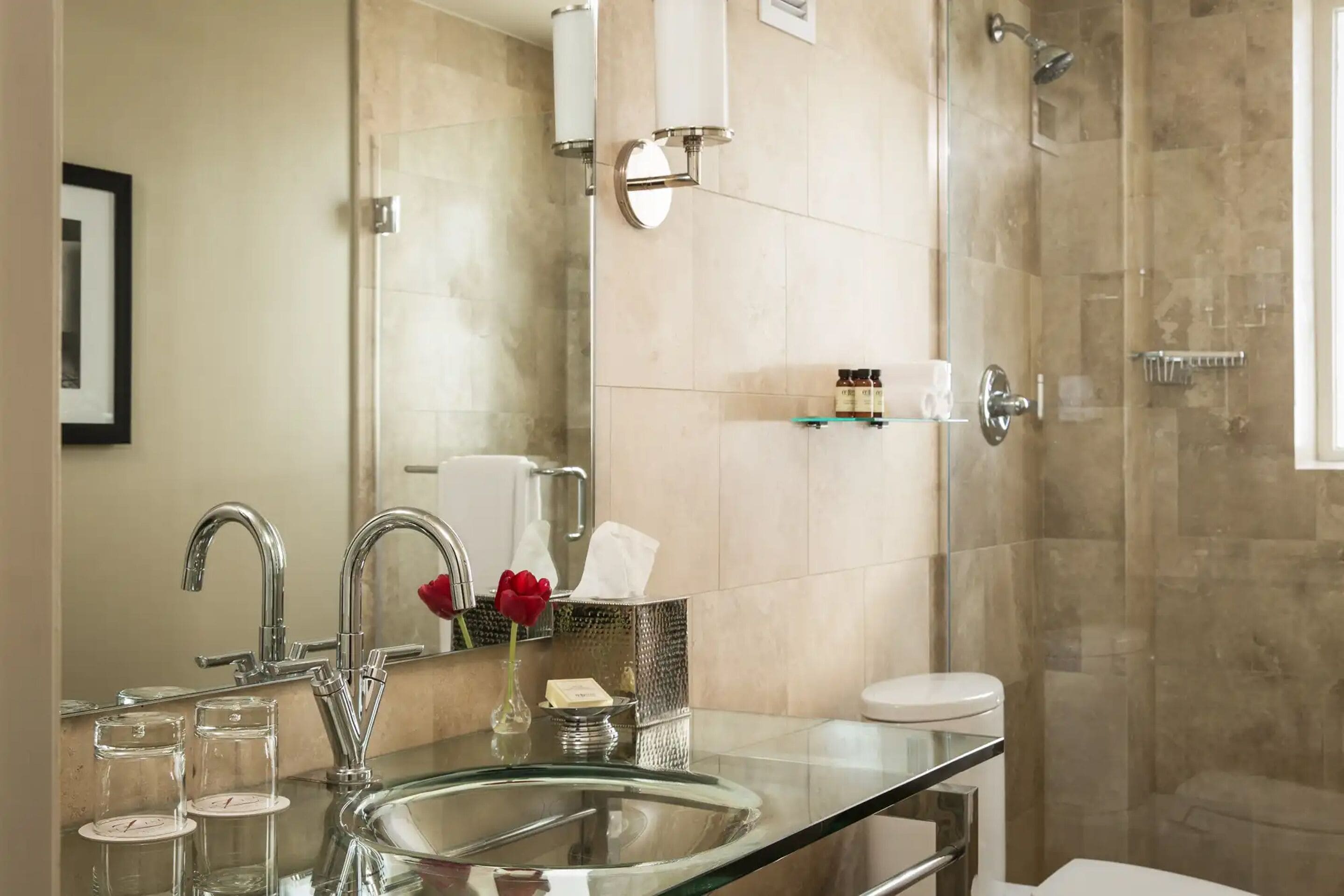 A modern bathroom with a glass sink, two faucets, a toilet, and a shower area.