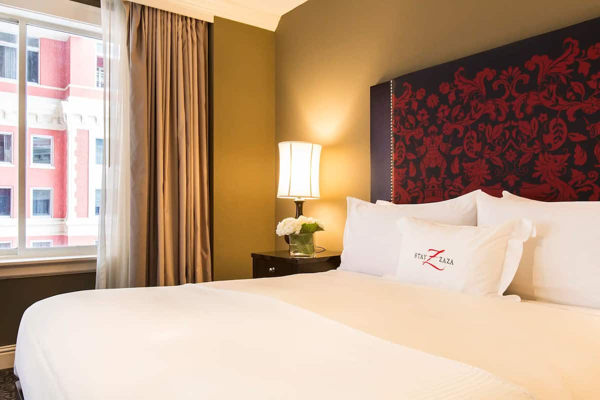 A hotel room with a large bed, a nightstand with a lamp and flowers, and a decorative wall.