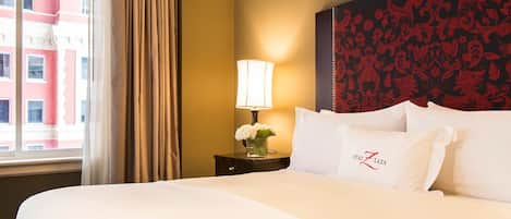 Ein Hotelzimmer mit einem großen Bett, einem Nachttisch mit Lampe und Blumen sowie einer Wand mit Dekoration.