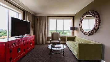 Ein Hotelzimmer mit einem großen Flachbildfernseher auf einer roten Kommode, einem grünen Sofa, einem runden Couchtisch und einem großen Spiegel an der Wand.