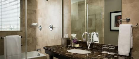 Un baño con ducha de vidrio, bañera, lavamanos de mármol y un espejo grande.