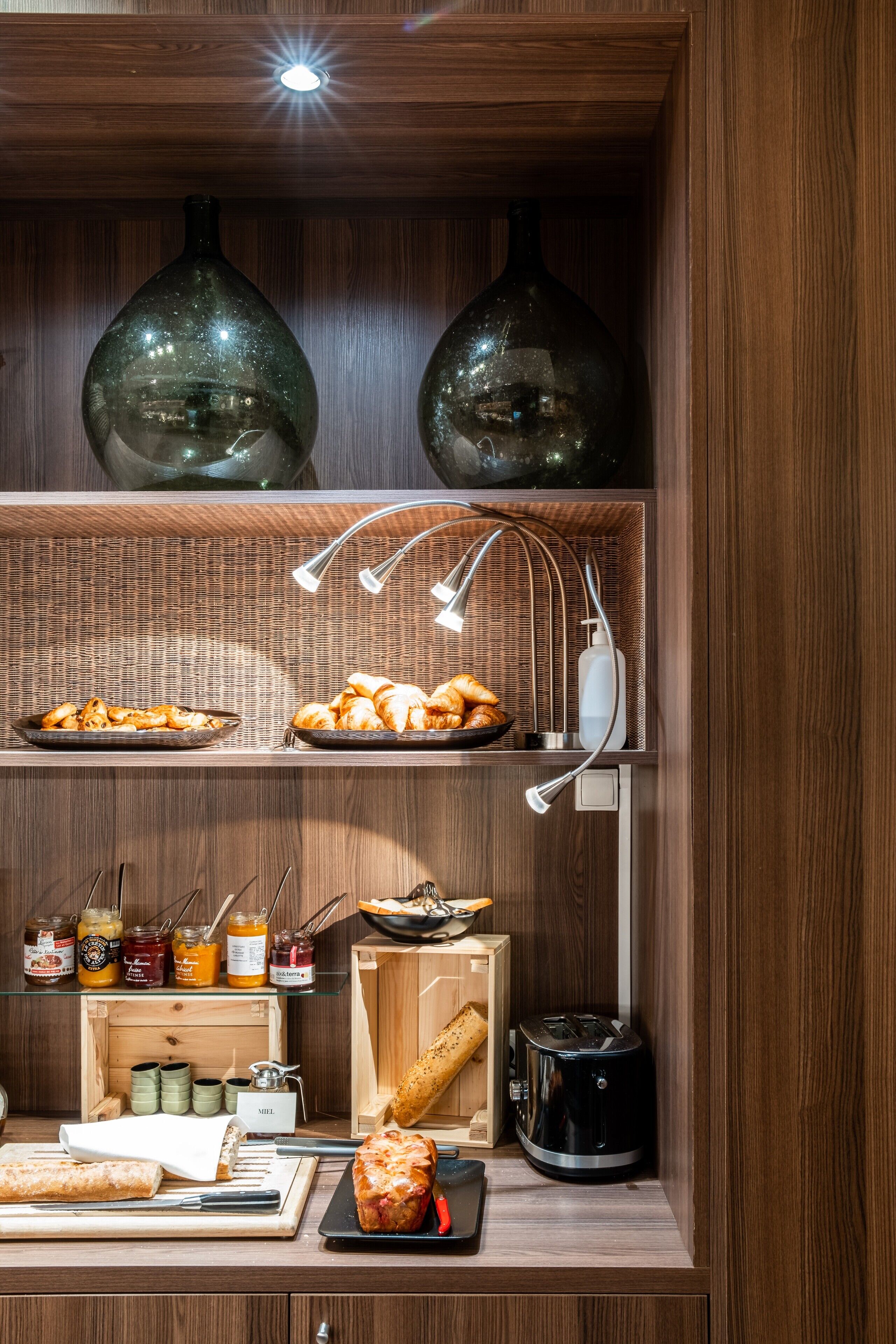 Una zona de cocina con armarios de madera, una exposición de pan, una máquina de café y varios frascos de condimentos.