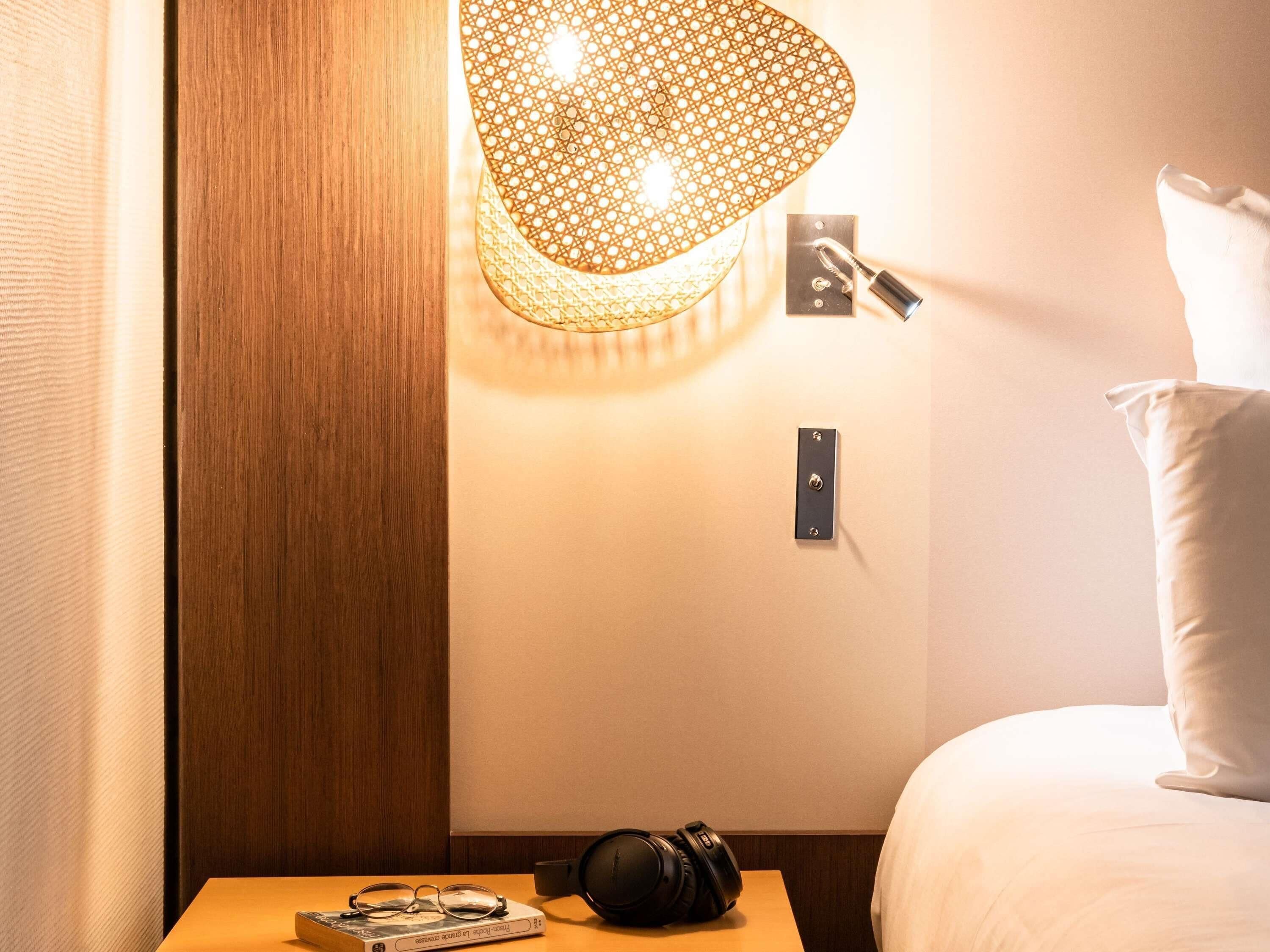A hotel room with a bed, a nightstand with a lamp, and a wall-mounted light fixture.