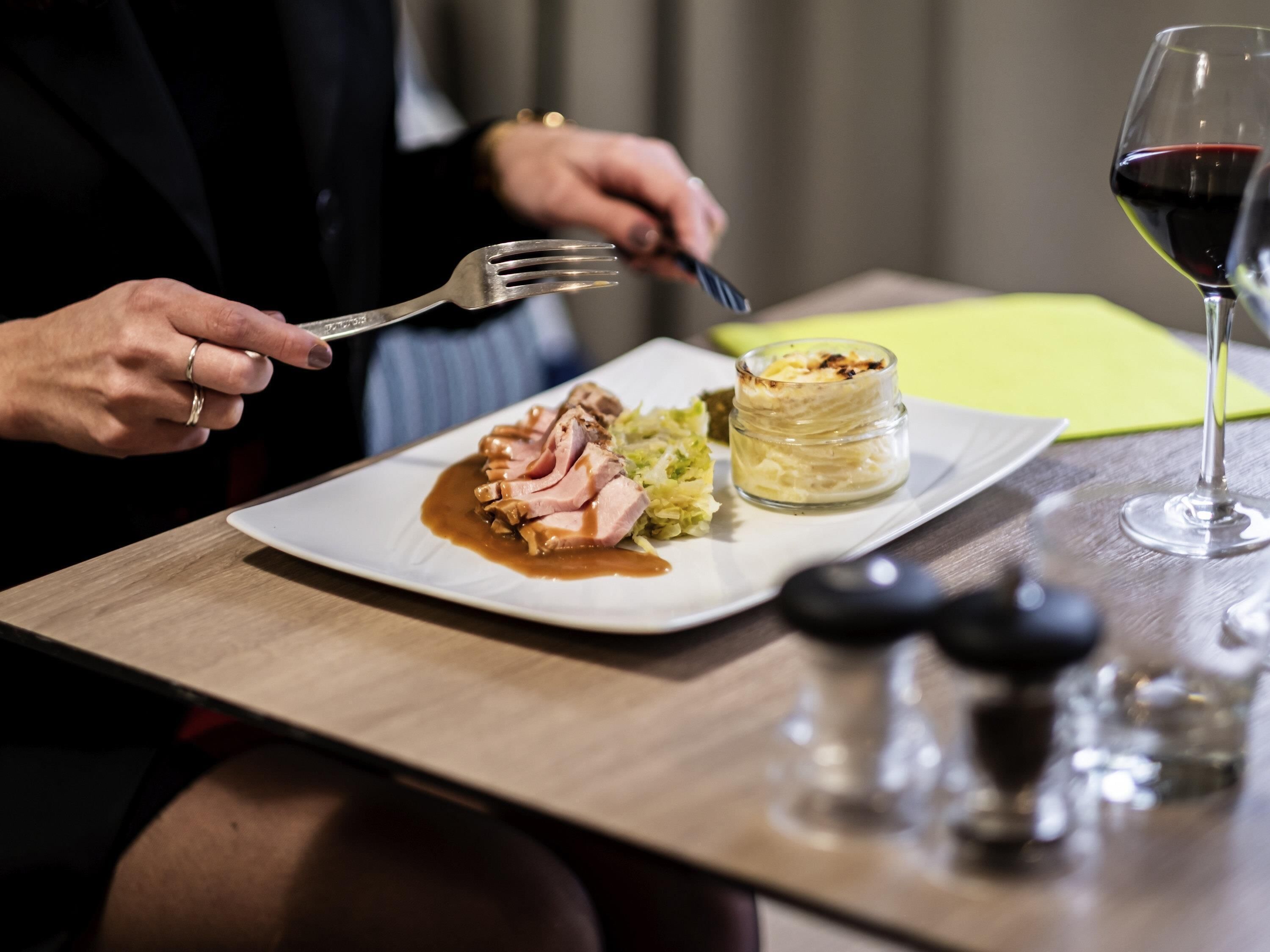 Una mesa de comedor con un plato de comida, una copa de vino tinto y salero y pimentero.