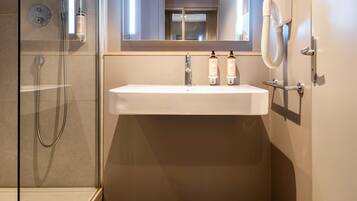 Un baño moderno con cabina de ducha de vidrio, un lavamanos blanco y dos botellas de champú, y un perchero para toallas.