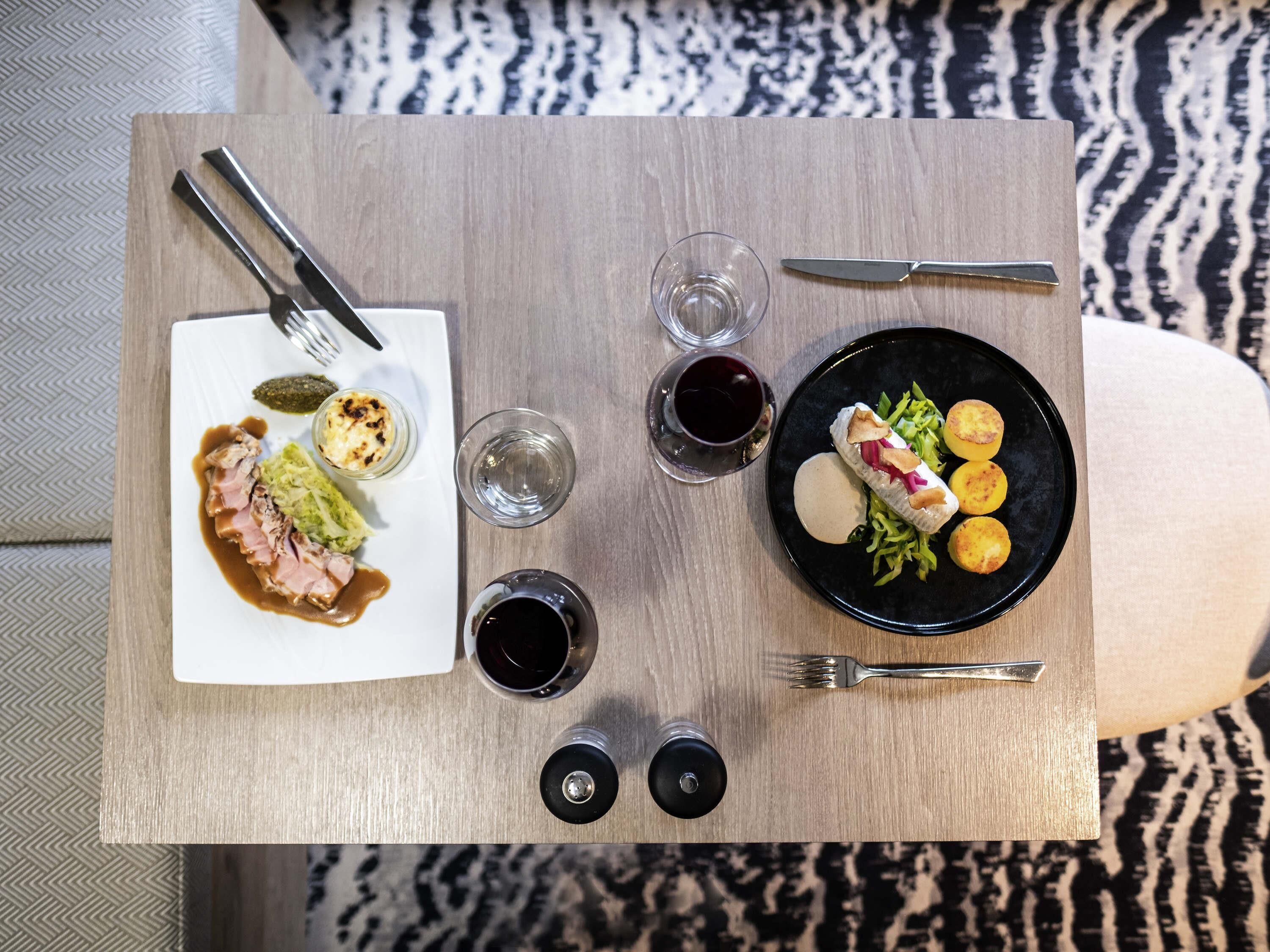 A dining table with a plate of food, a glass of red wine, and a fork.