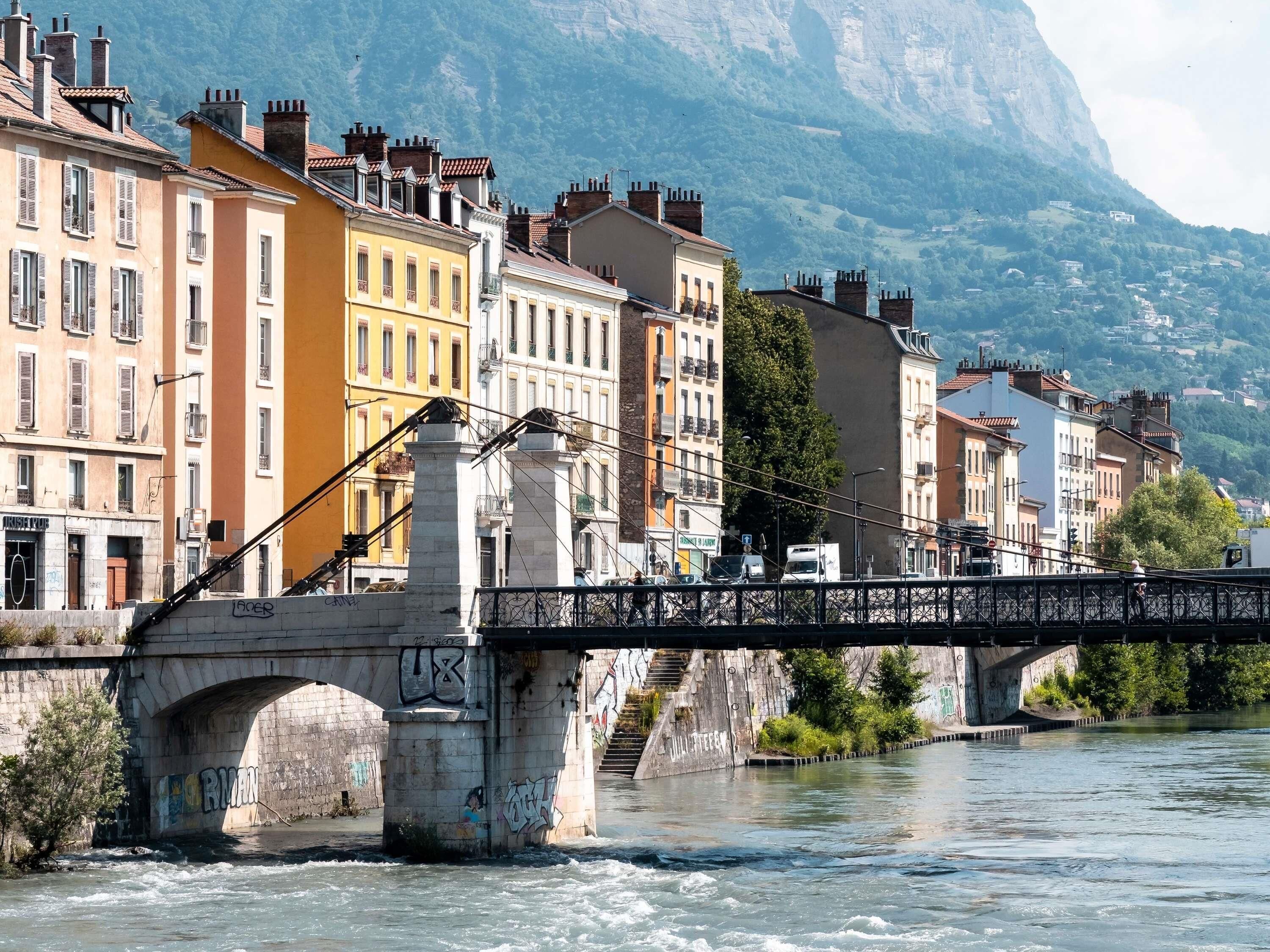 A stone bridge over a river with buildings on either side and a mountain in the background.