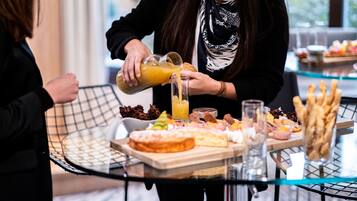 Une personne verse du jus d’orange dans un verre sur une table où se trouvent divers aliments et un verre d’eau.