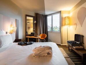 Een hotelkamer met een bed, een bureau, een stoel, een lamp en een koffer.