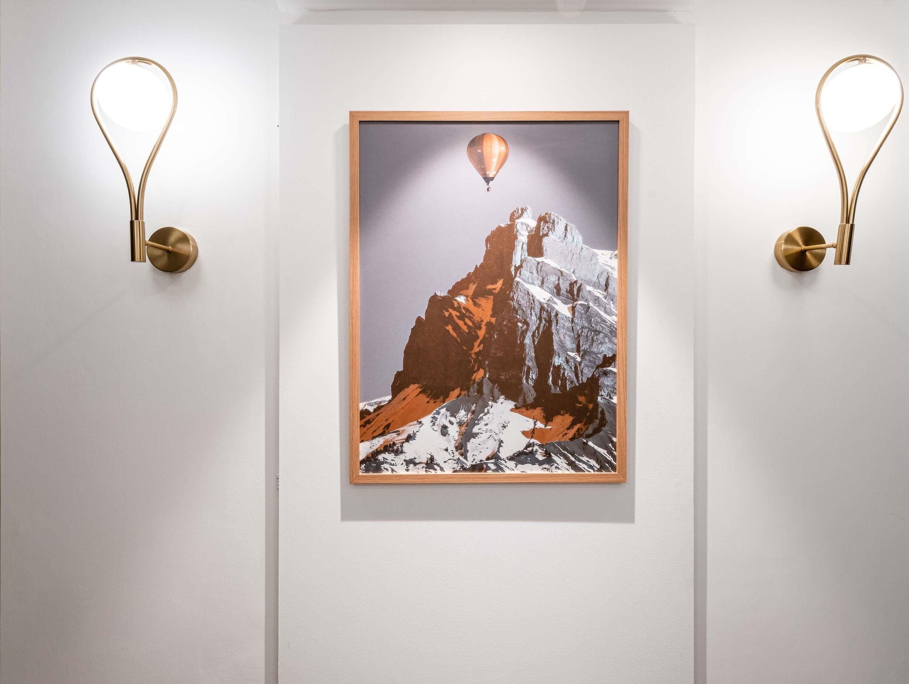 Une œuvre d’art encadrée représentant un sommet de montagne survolé par un ballon à air chaud, et flanquée de deux appliques murales.