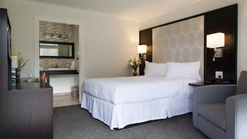 A hotel room with a large bed, a desk, a chair, a nightstand, a lamp, and a mirror.