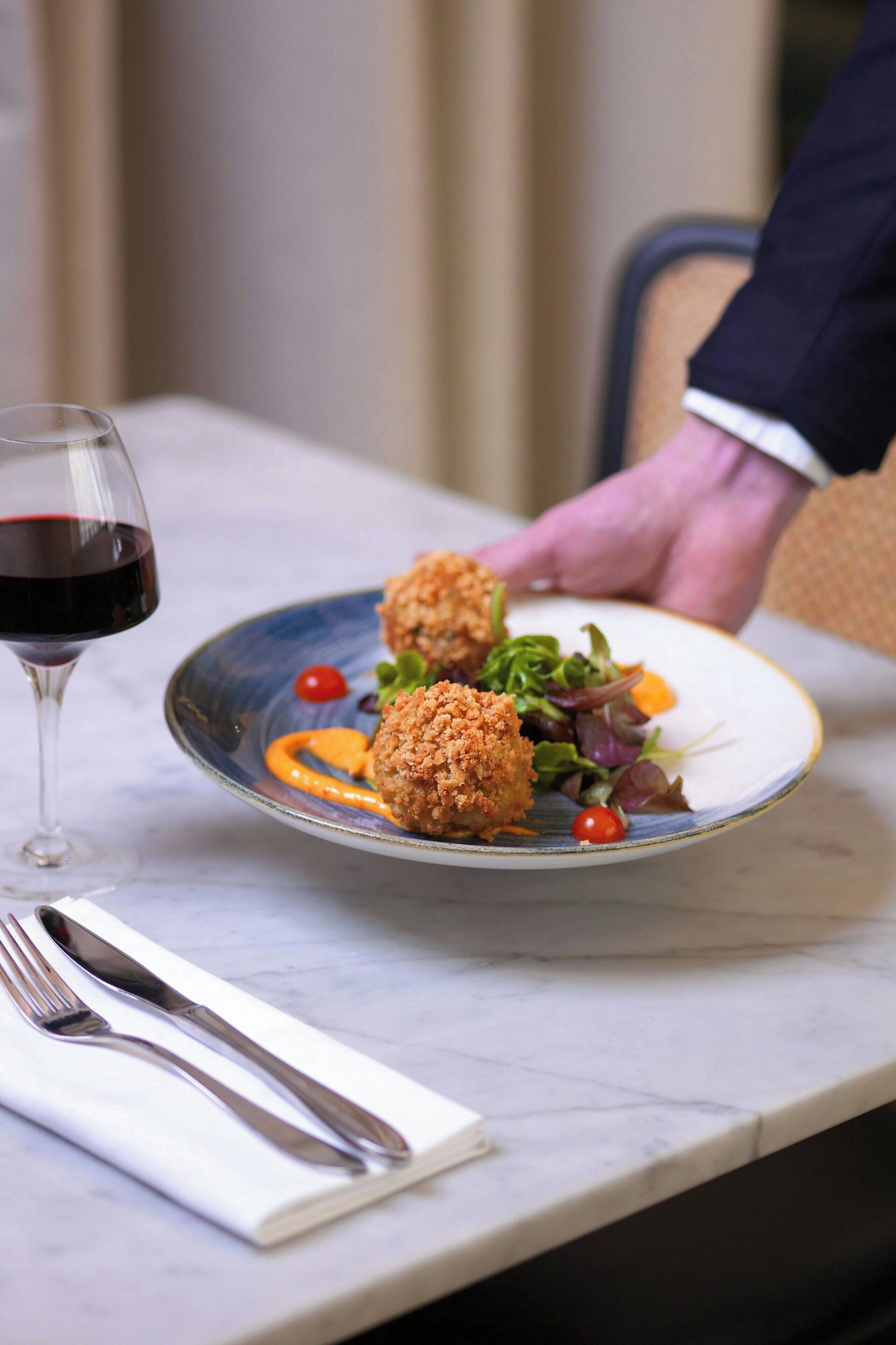A plate of food with a glass of red wine on a table.