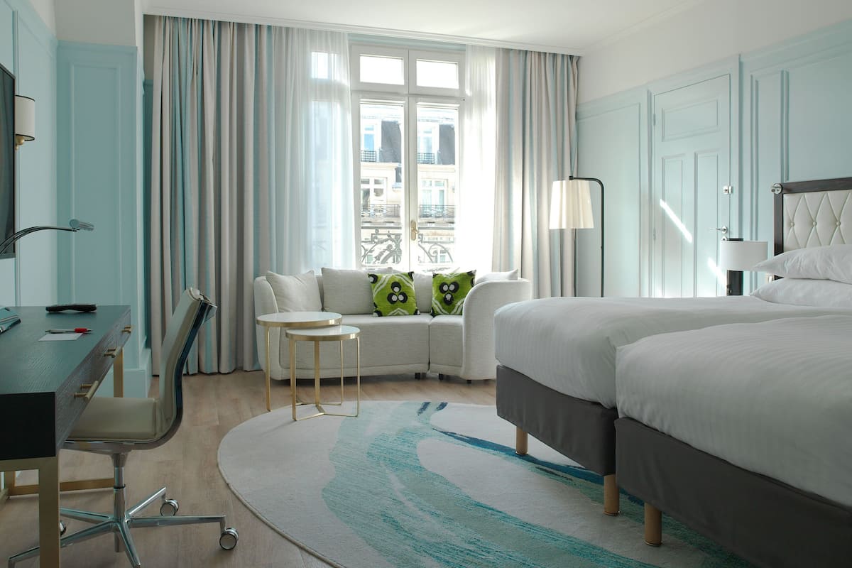 A hotel room with a desk, two beds, a sofa, and a view of the city.