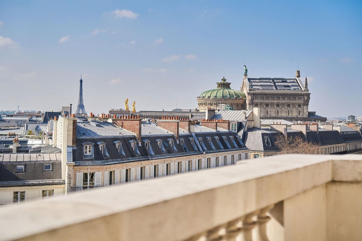 A view of Parisian rooftops with the Eiffel Tower and the Louvre Pyramid in the background.