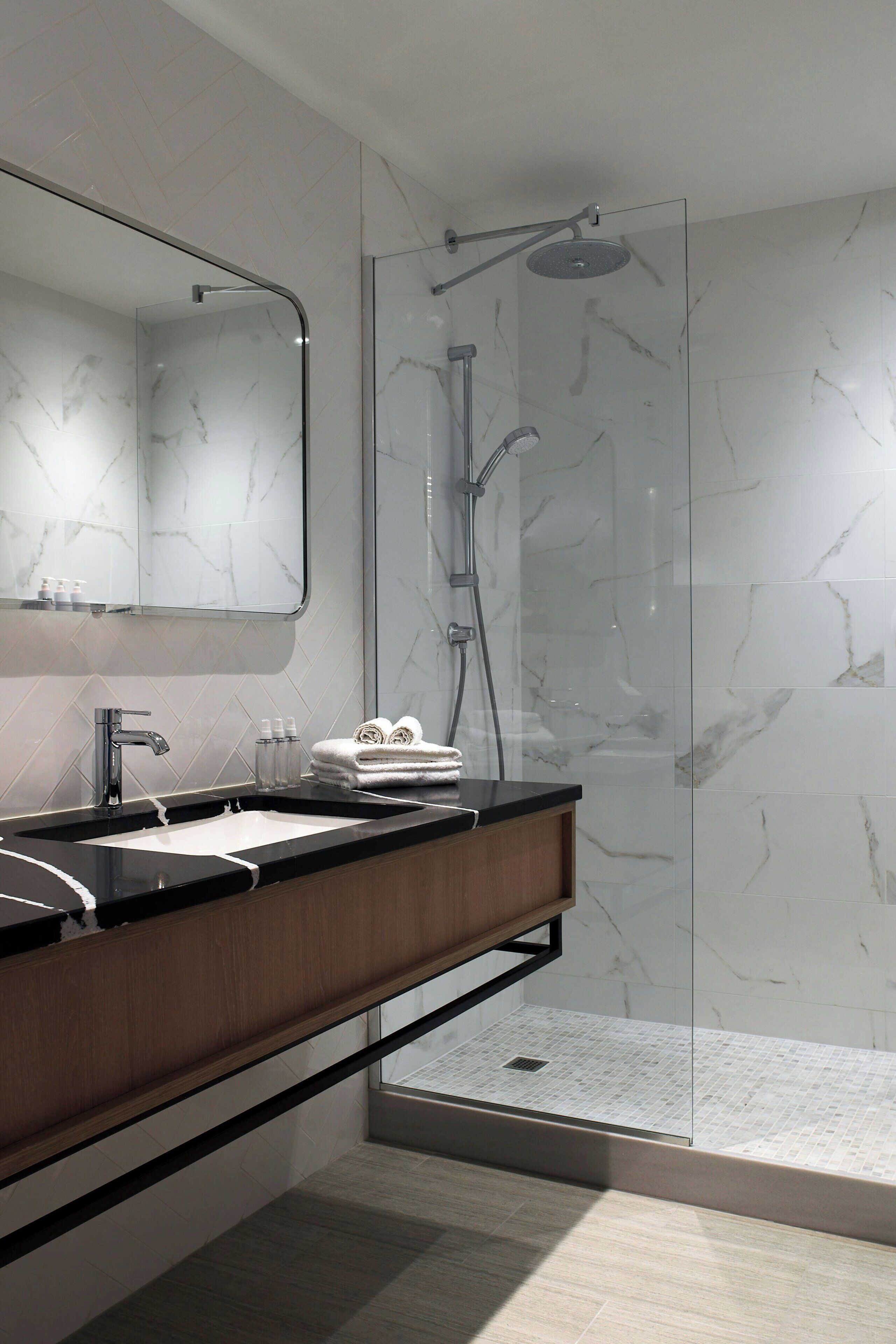 Ein modernes Badezimmer mit einer in Glas abgeschirmten Dusche, einem Holzwaschtisch mit schwarzer Arbeitsplatte und einer Marmor-Spritzschutzwand.