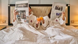 Two people in a hotel room, each holding a newspaper and a glass of orange juice, with a tufted headboard behind them. - Paris Marriott Opera Ambassador (Paris)