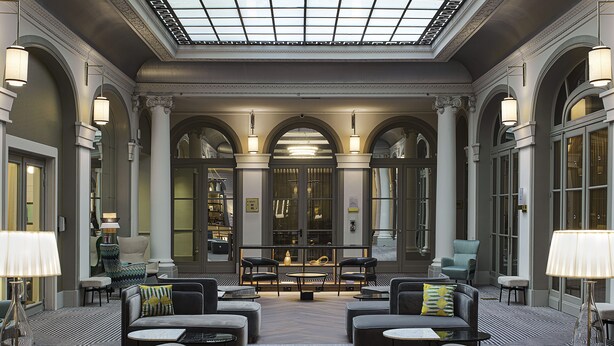 A spacious lobby with a high ceiling and skylight, featuring a central seating area with sofas and armchairs, a marble coffee table, and a reception desk. - Paris Marriott Opera Ambassador (Paris)