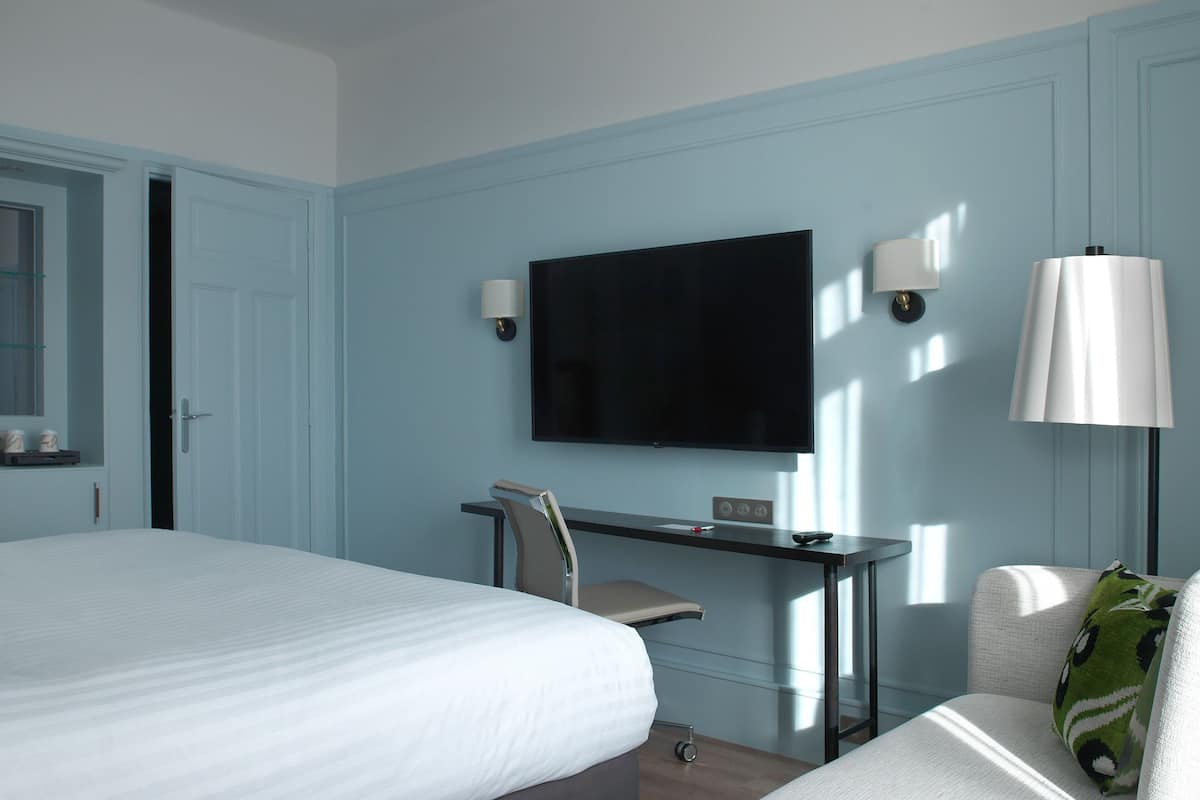 A hotel room with a bed, a desk with a chair, a TV, and two wall-mounted lamps.