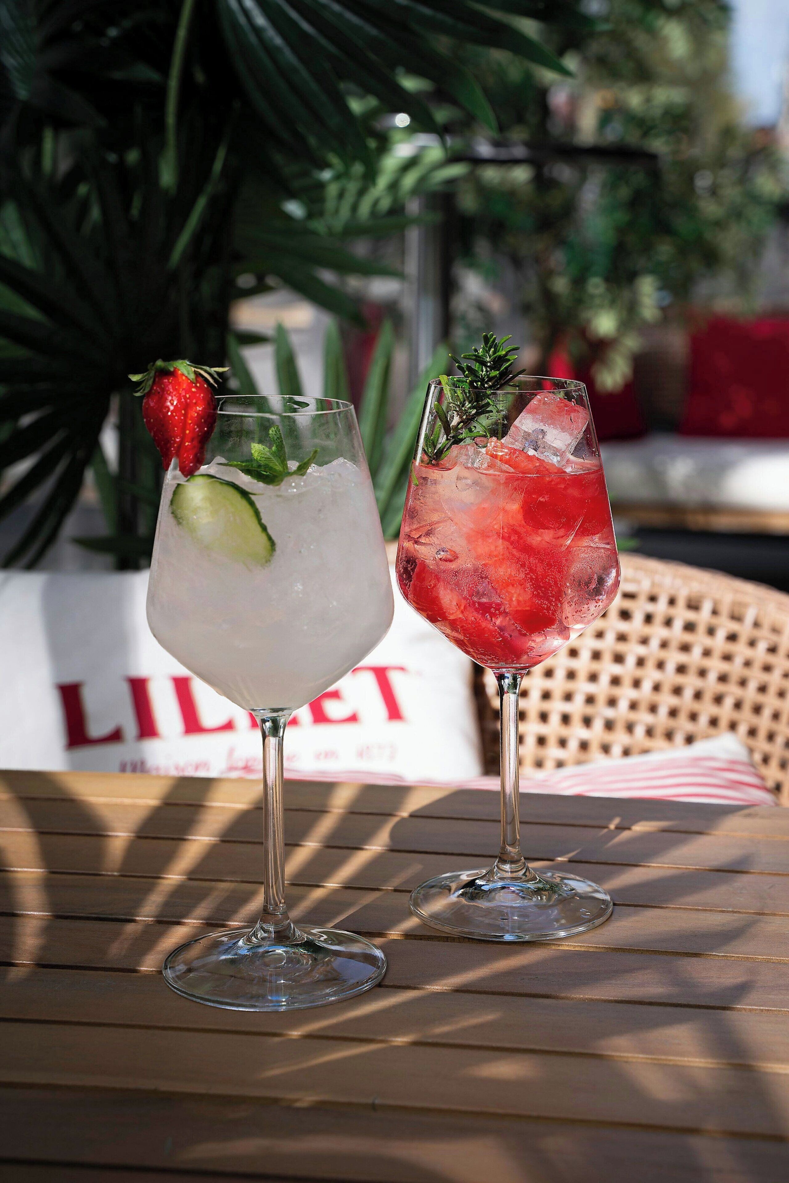 Twee drankjes op een tafel, met een rieten stoel en een bord in de achtergrond.