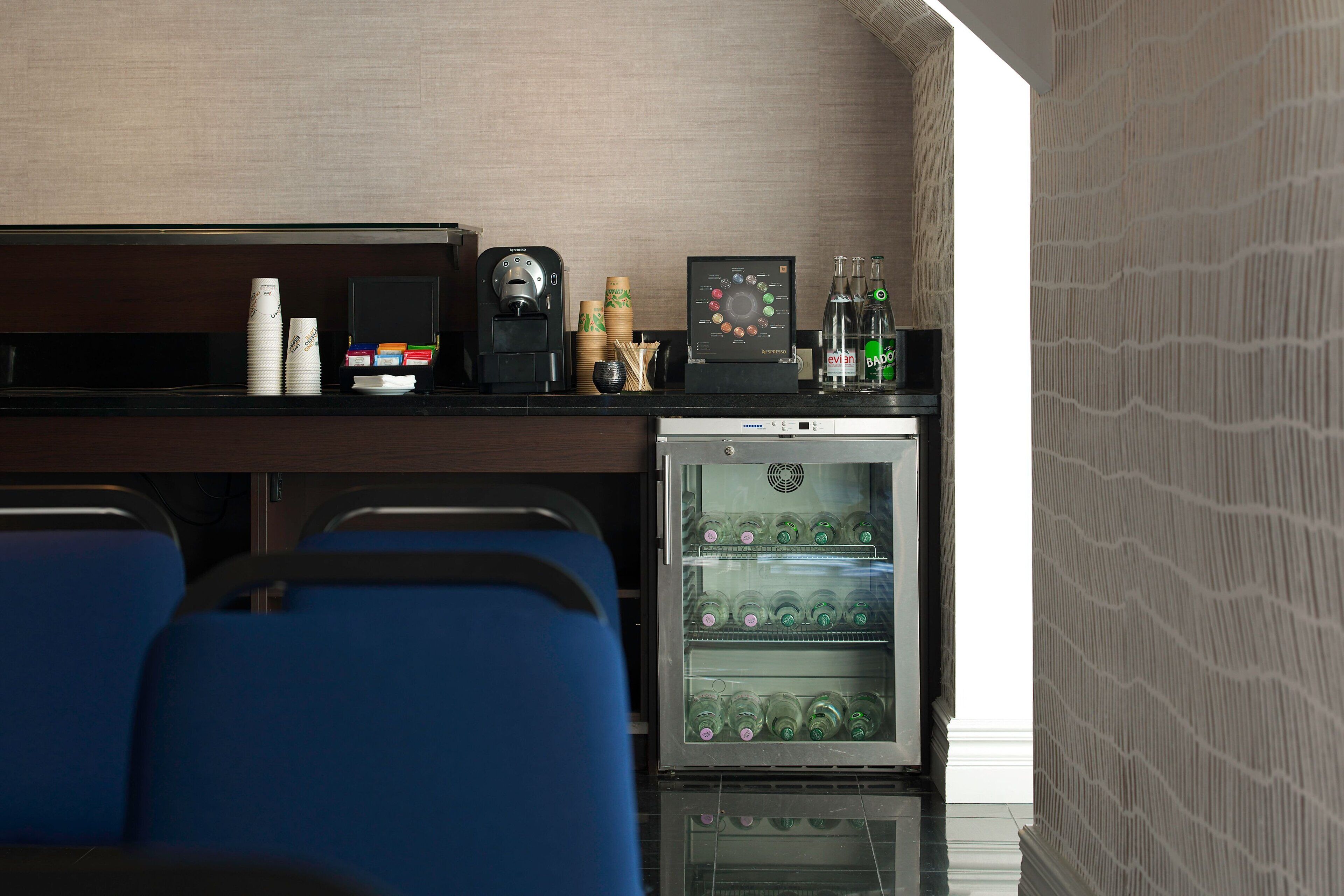 A compact hotel room with a minibar, a coffee machine, and a refrigerator stocked with beverages.