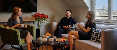 A modern living room with a city view, a flat-screen TV, and a dining table with breakfast items.
