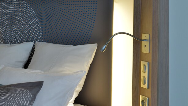 A neatly made bed with white and patterned pillows, a wooden headboard, and a bedside table with a lamp.