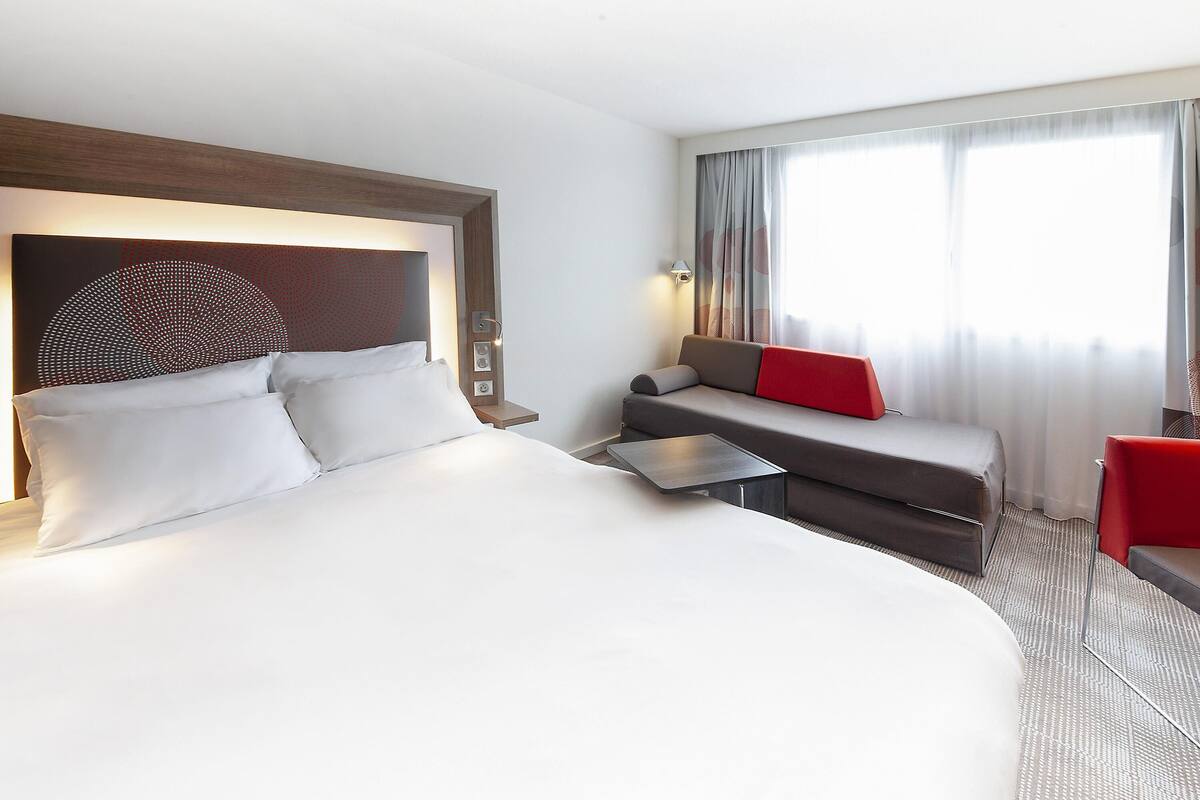 A modern hotel room with a large bed, a sofa, a small table, and a desk.