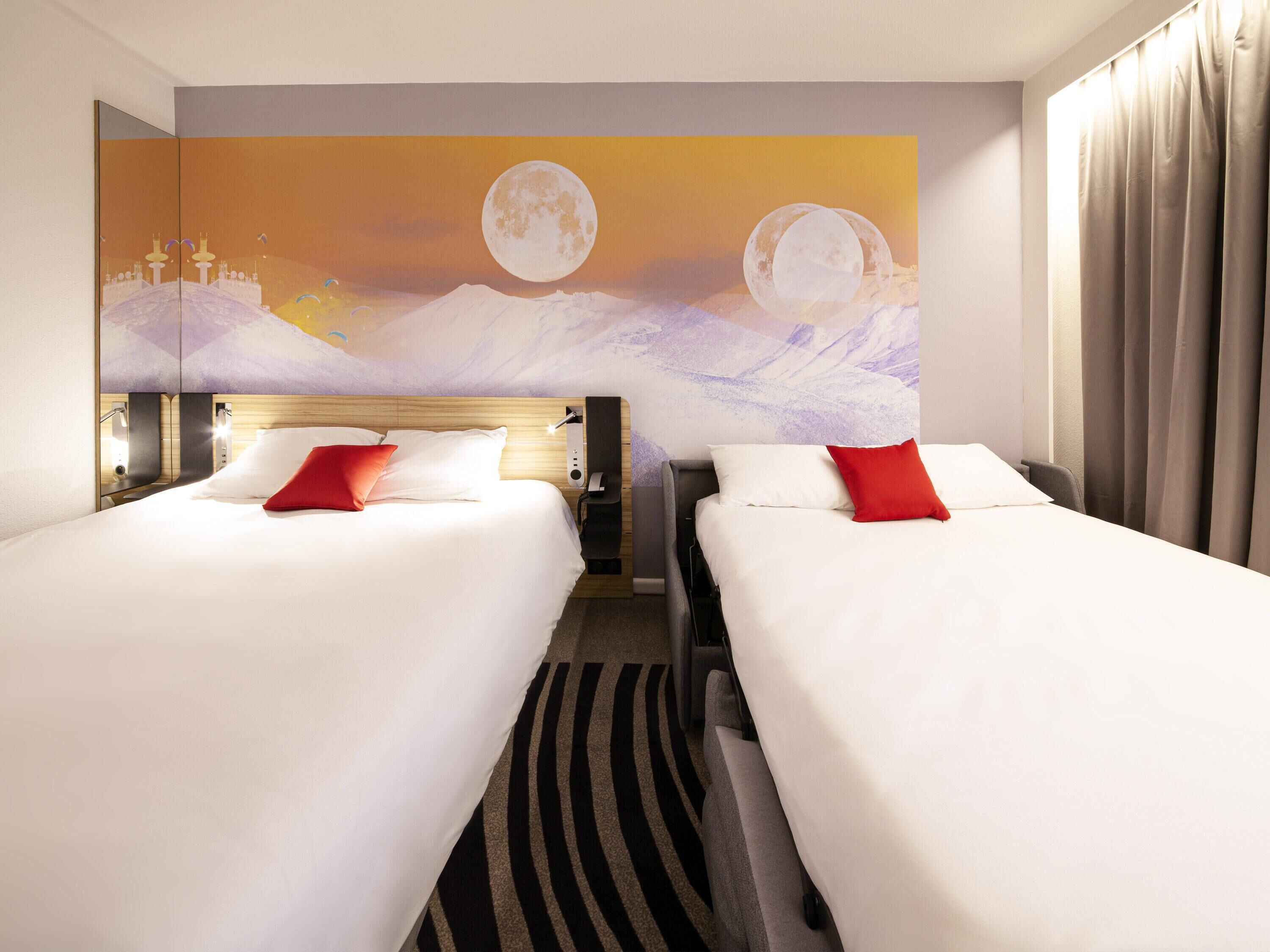 A hotel room with two beds, a large wall mural of a moonlit landscape, and a view of the mountains.