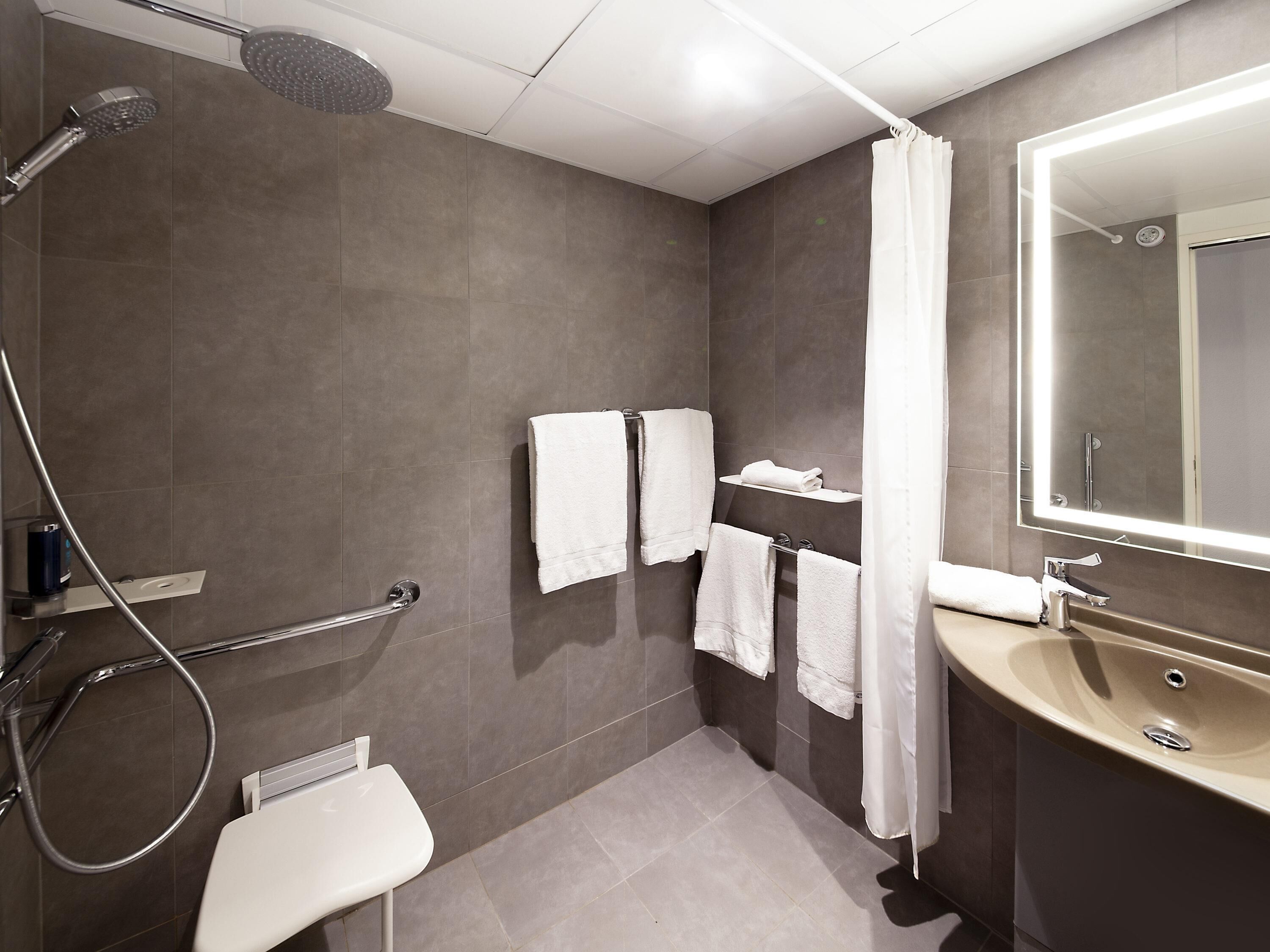 A modern bathroom with a shower, a toilet, a sink, and a mirror.