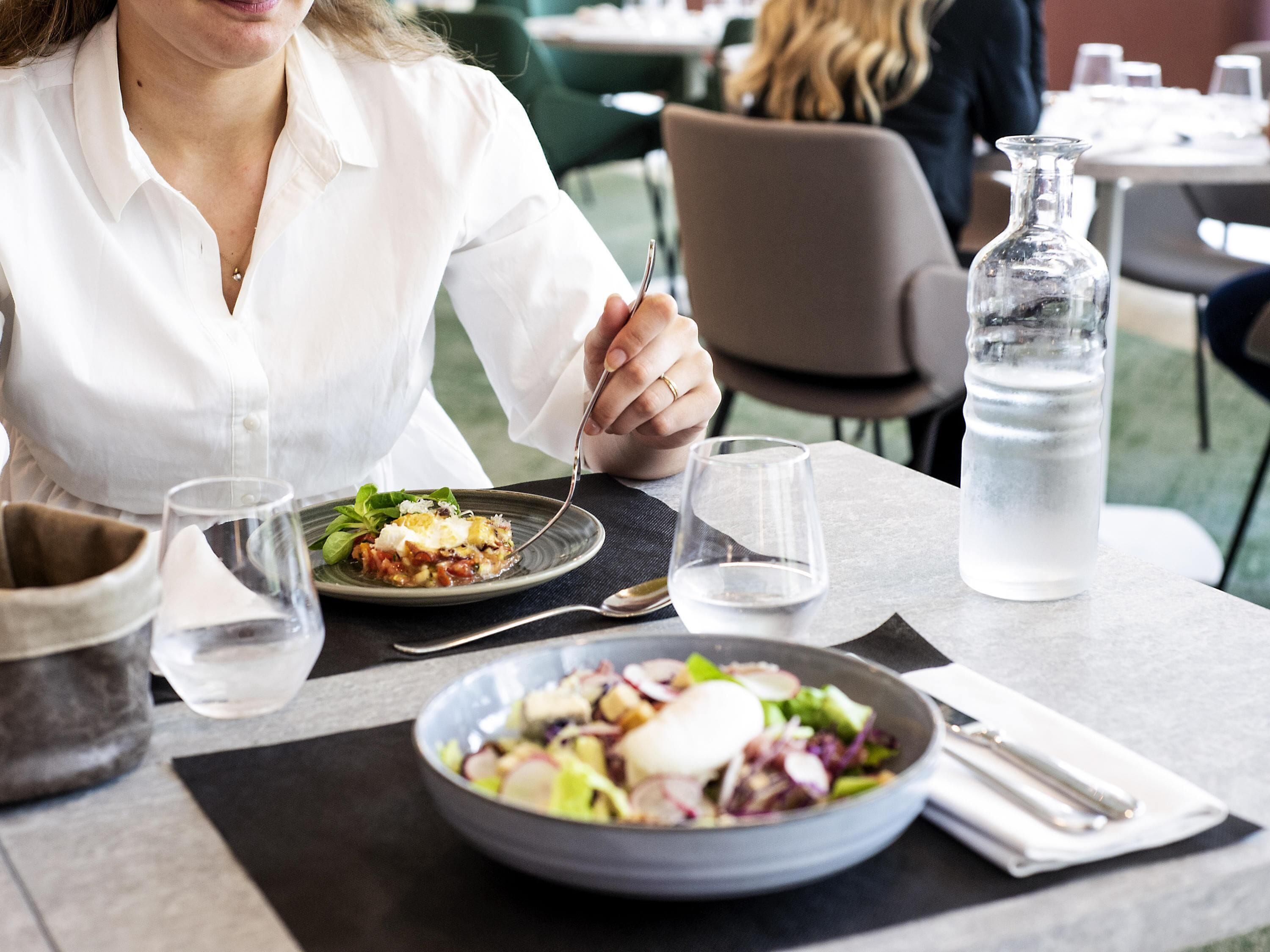 Une table à manger avec une assiette de nourriture, un verre d’eau, une bouteille d’eau et un stylo posés sur une serviette.