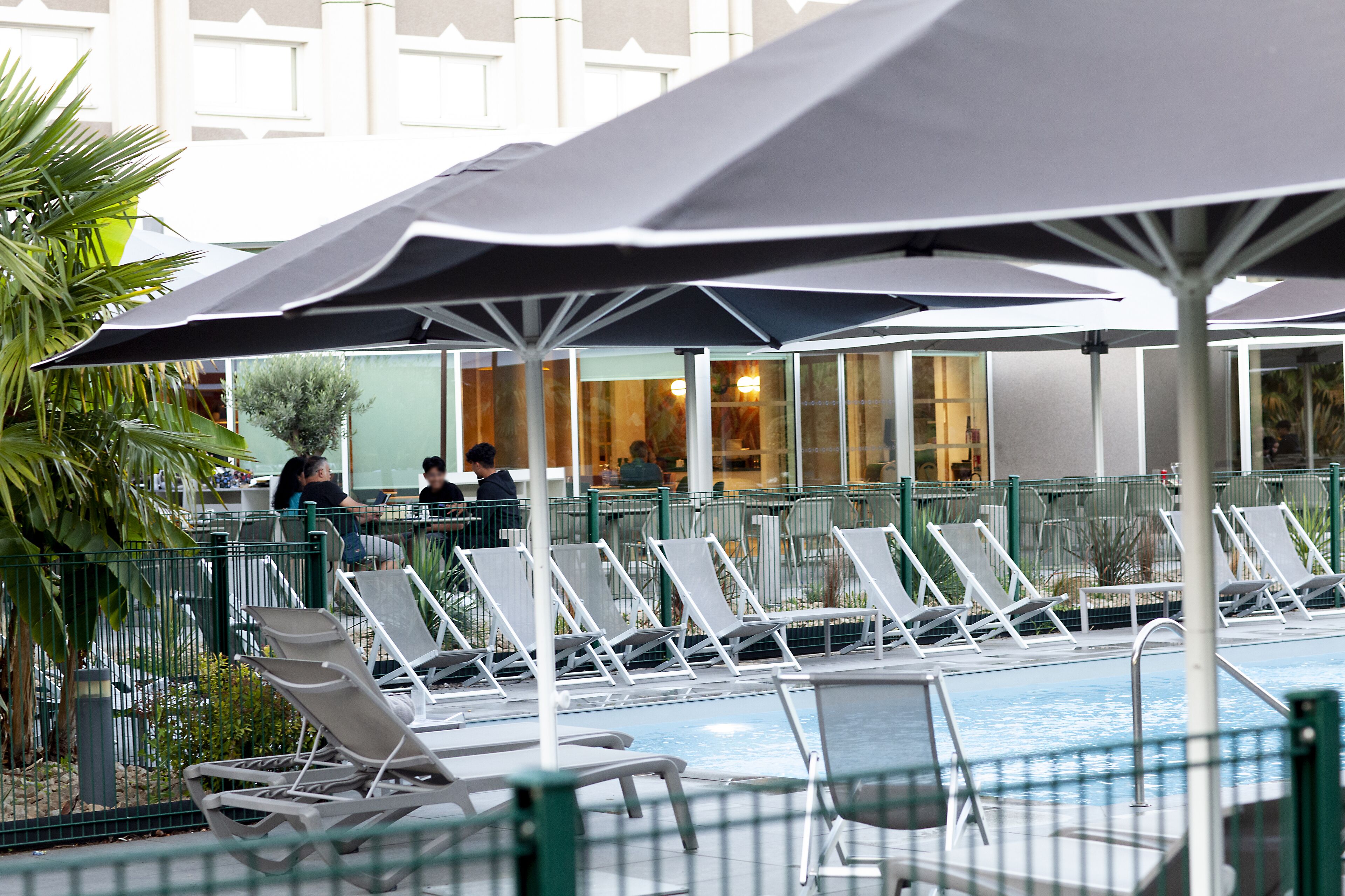 A poolside area with lounge chairs and umbrellas, a pool, and a building in the background.