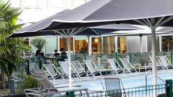 A poolside area with lounge chairs and umbrellas, a pool, and a building in the background.