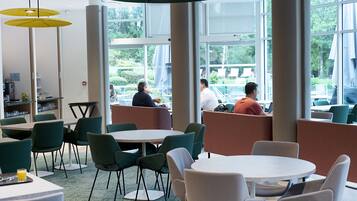 A modern dining area with round tables and green chairs, large windows, and a view of the outdoors.