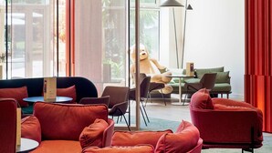 Un interior moderno con asientos tapizados en rojo, un gran oso de peluche sobre una mesa y vistas al exterior con vegetación.