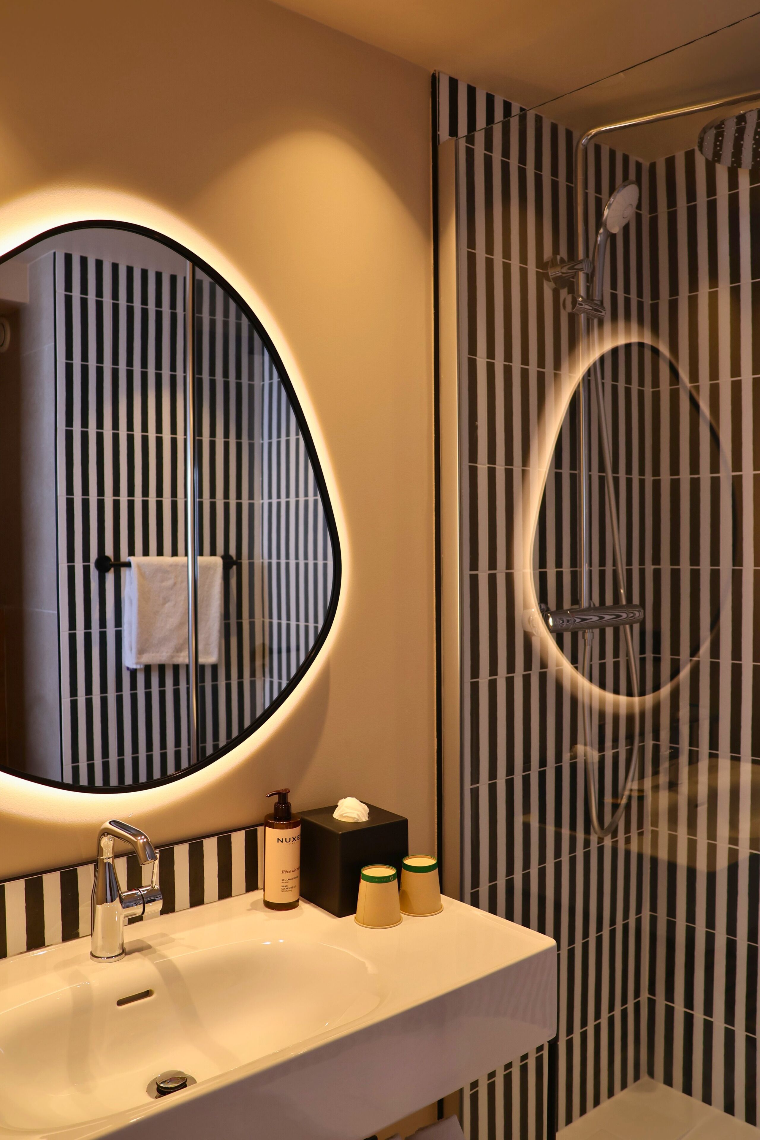 A bathroom with a round mirror, a sink, a handheld showerhead, and striped tiles.