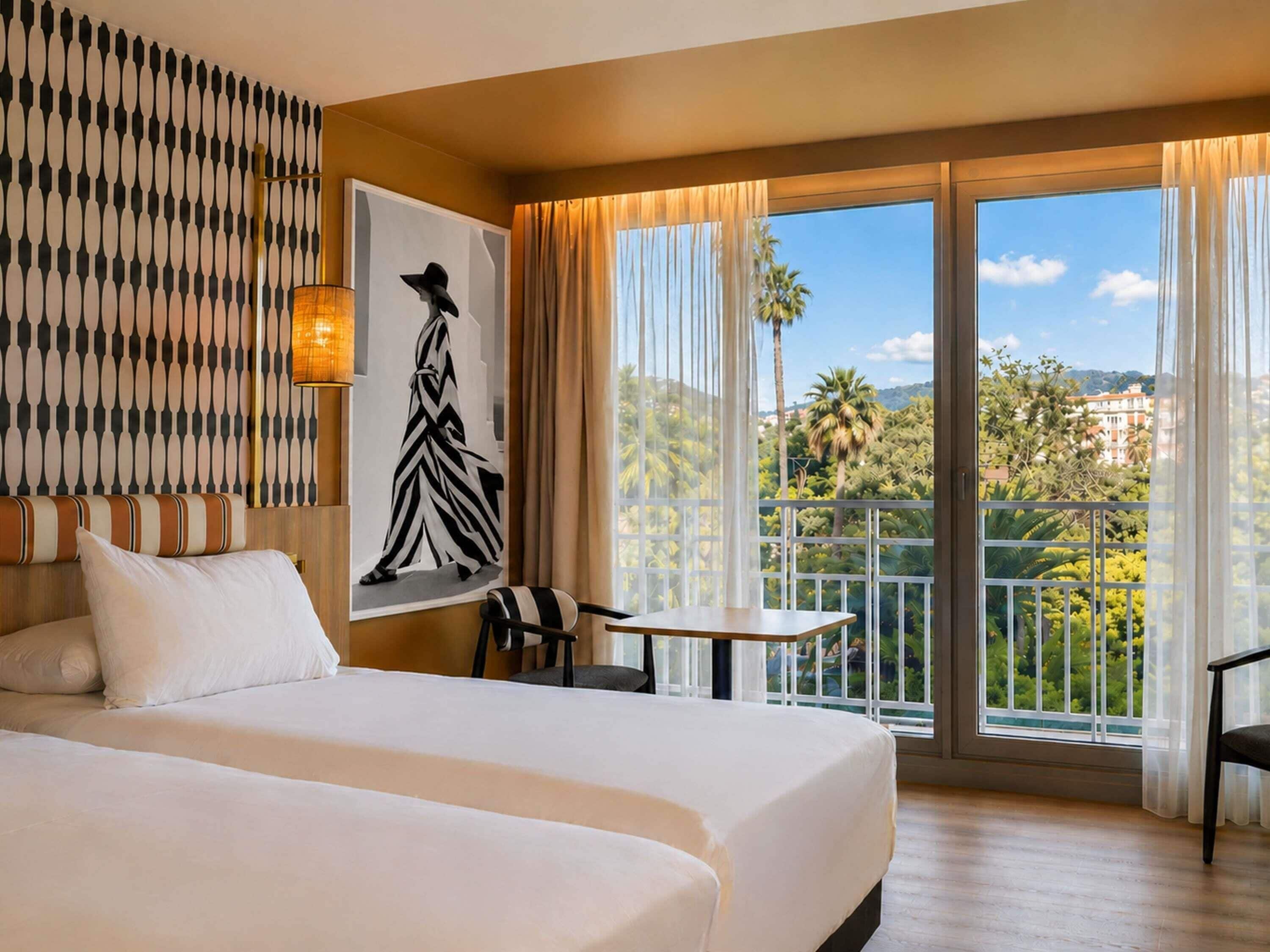 A hotel room with a large bed, a painting, a table, and a balcony with a view of palm trees and buildings.