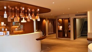 A reception area with a curved white counter, hanging pendant lights, wooden panel walls, and a staircase in the background.