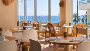 A restaurant with large windows, wooden tables, and chairs, overlooking the ocean.