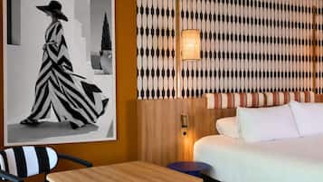 Habitación de hotel con cama, una mesita, una silla, pared con diseño decorativo y un cuadro en la pared.