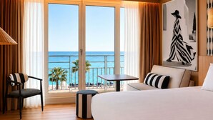 A hotel room with a large bed, a chair, a small table, and a view of the ocean.