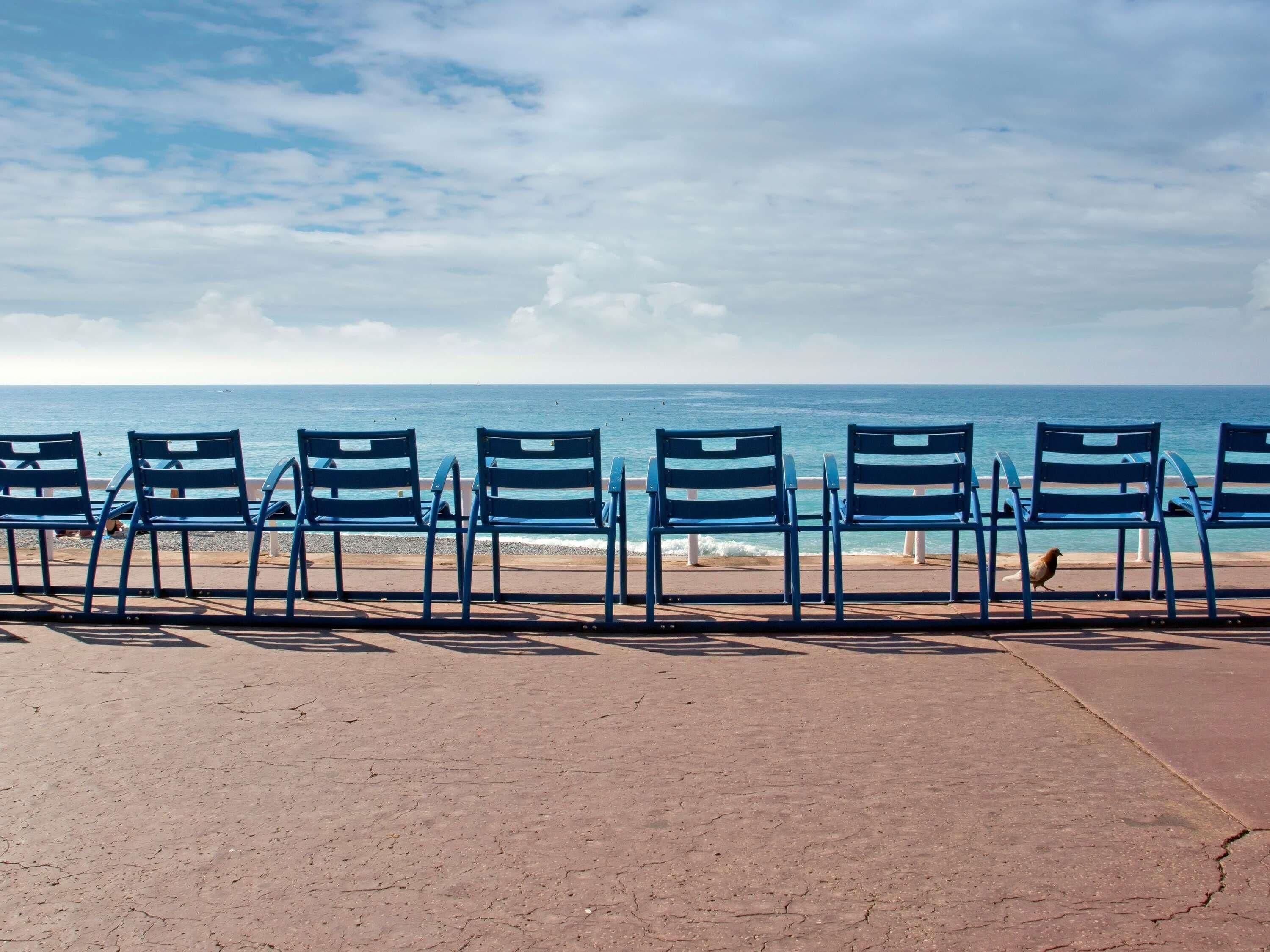 A row of blue chairs facing the ocean.