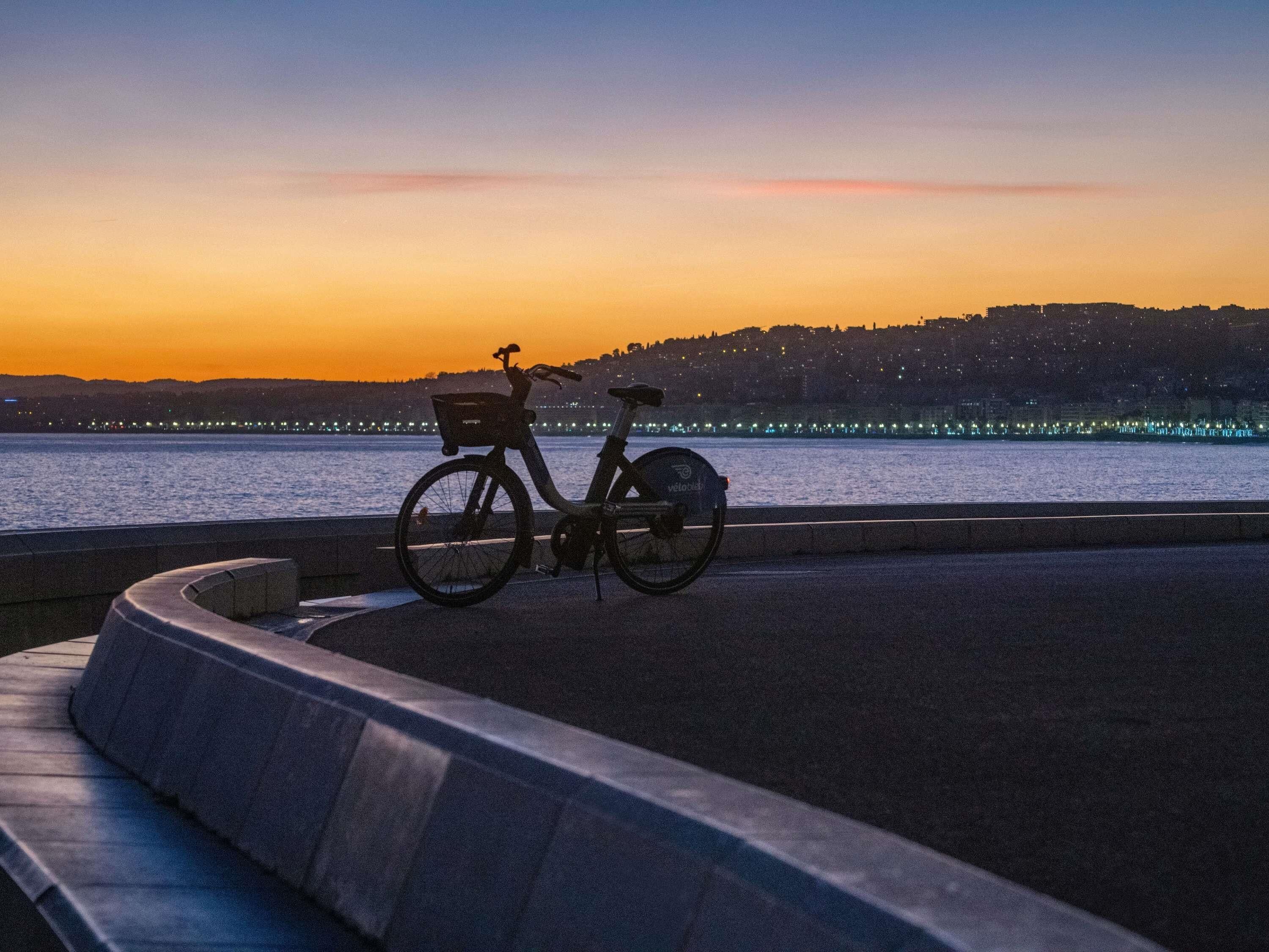 A bicycle parked by a waterfront with a sunset in the background.