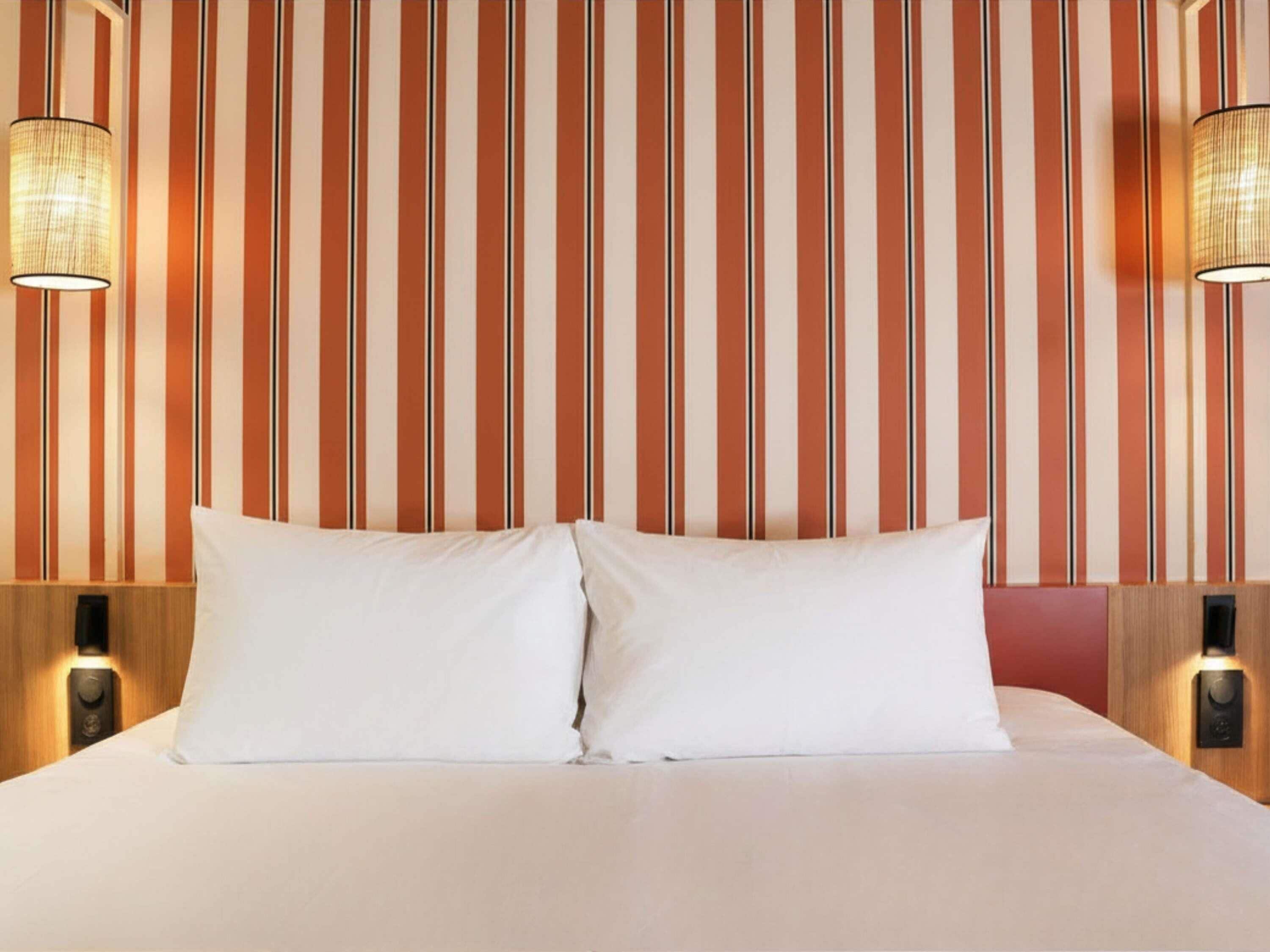 A hotel room with a striped wallpaper, two bedside lamps, and a bed with white bedding.