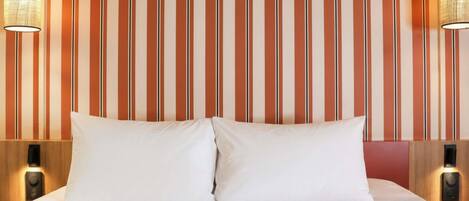 A hotel room with a striped wallpaper, two bedside lamps, and a bed with white bedding.