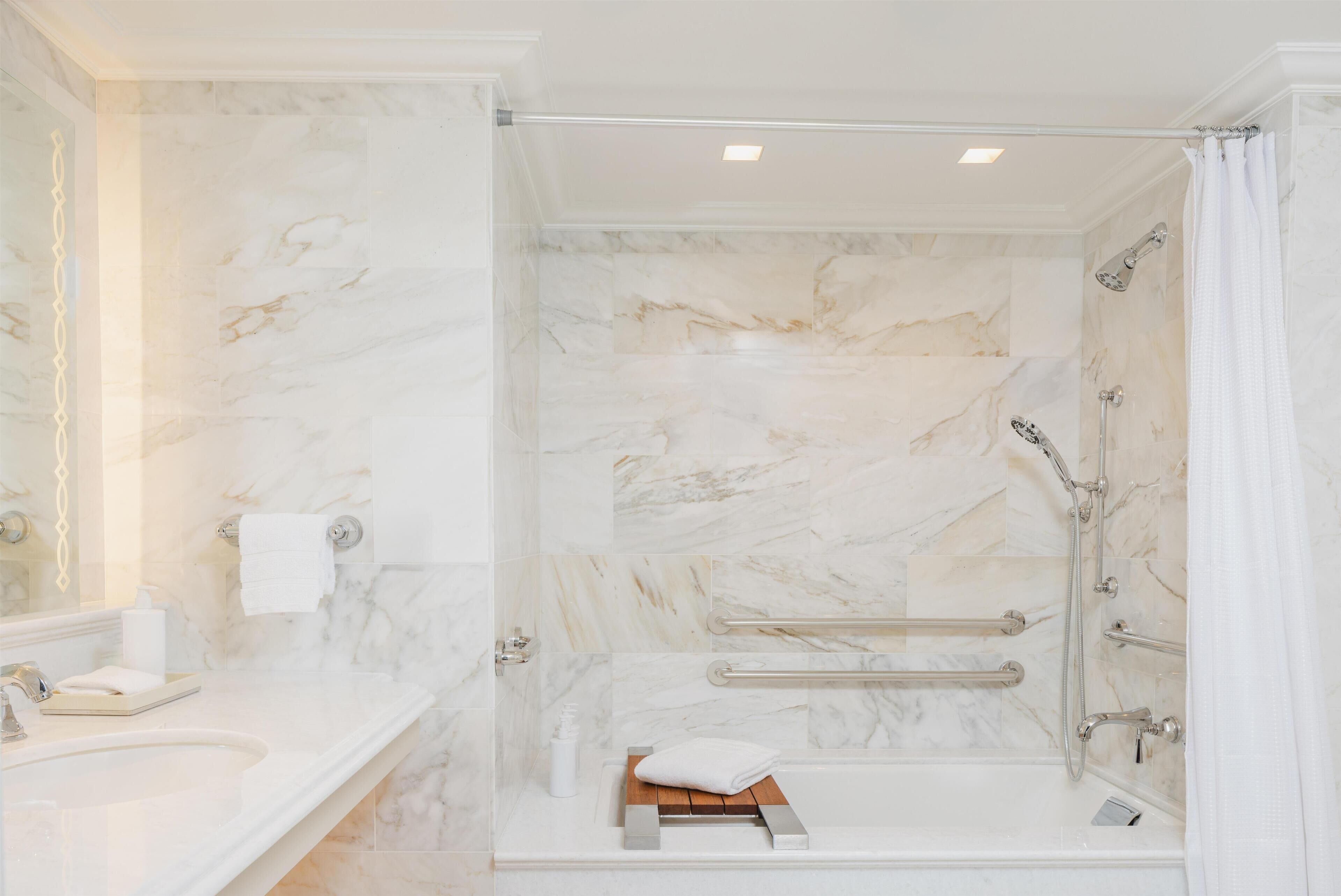 A bathroom with a marble wall, a sink, a shower with grab bars, and a towel rack.