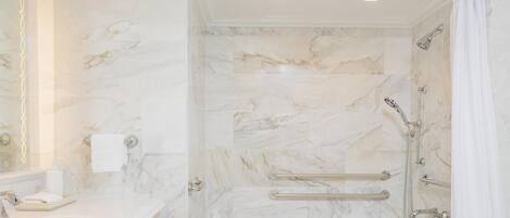 A bathroom with a marble wall, a sink, a shower with grab bars, and a towel rack.